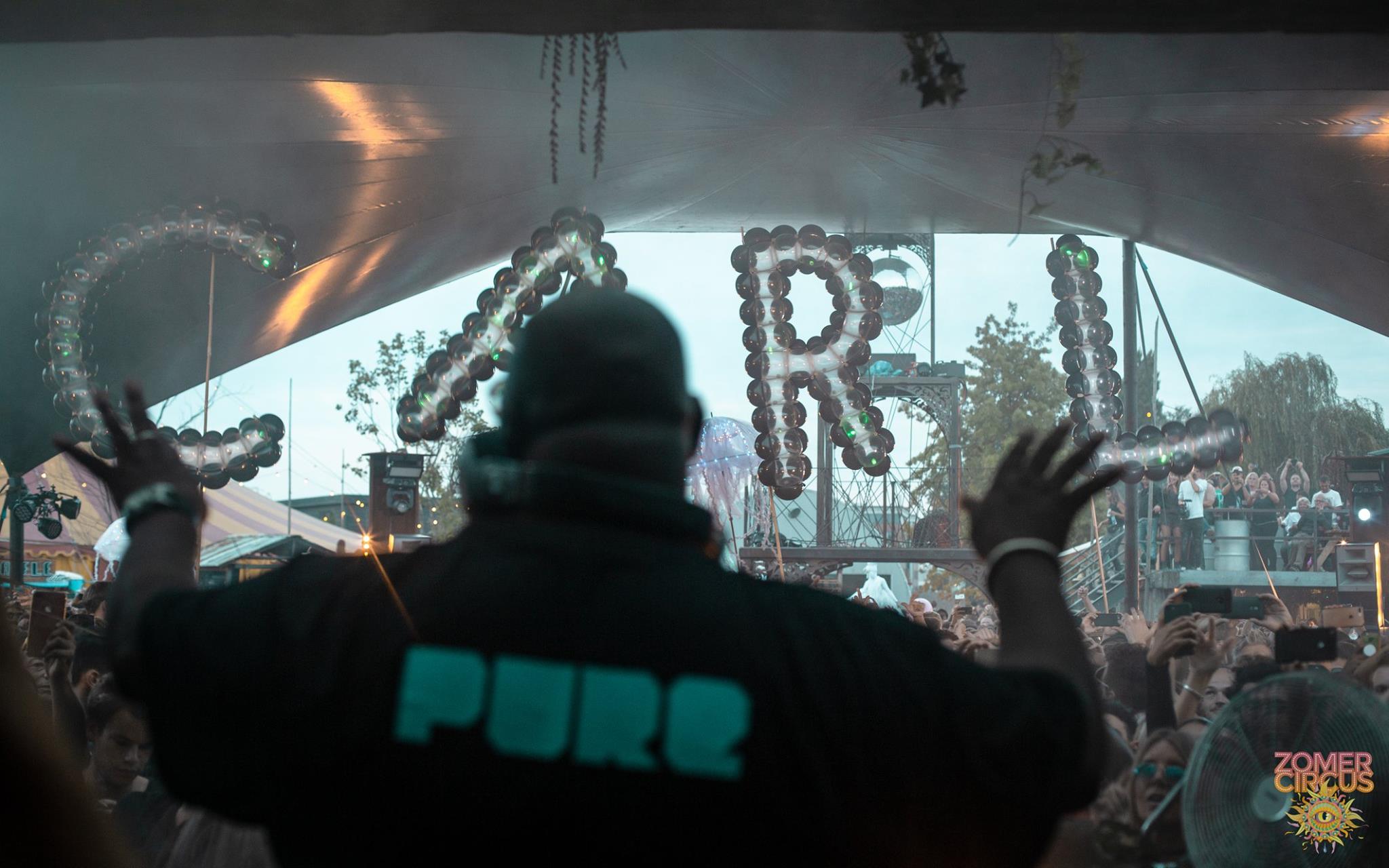 Carl Cox in a 'PURE' jacket facing the giant illuminated 'CARL' LED balloon letters above the crowd at Zomer Circus, Thuishaven Amsterdam, 2018 — Spellbound by Out of Thin Air