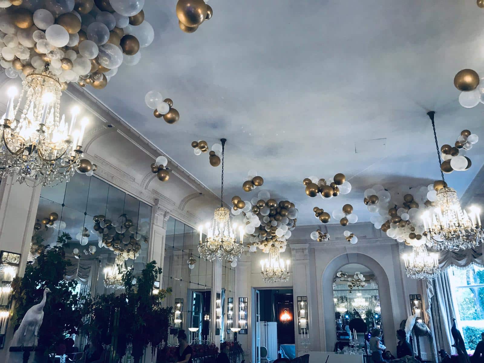 Custom gold and white balloon ceiling clusters and chandelier decorations at an unknown venue (2019)