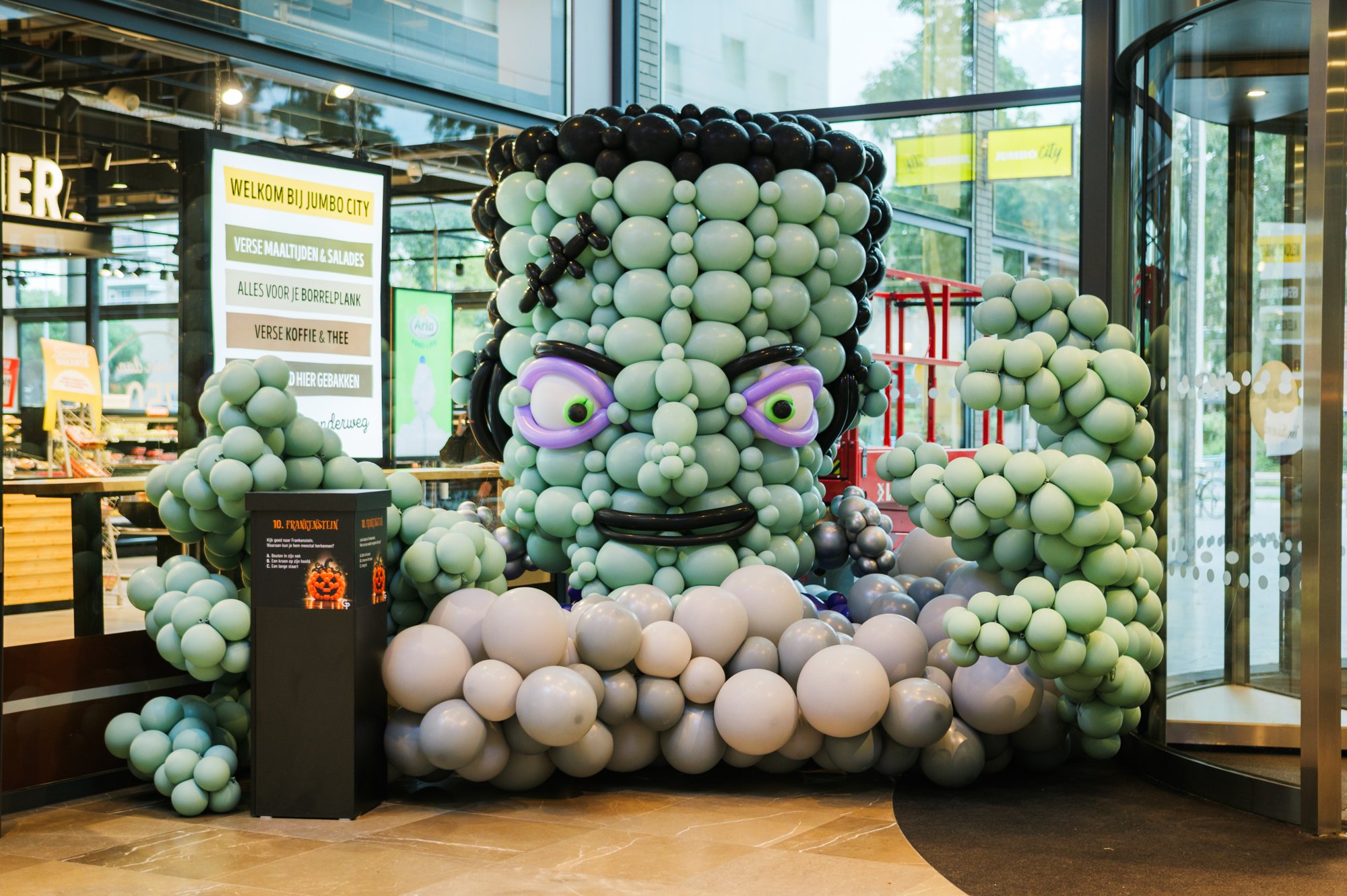 Green balloon Frankenstein head at the entrance of Gelderlandplein (2026) — Design: Gijs de Smed — Photo: zestien:negen