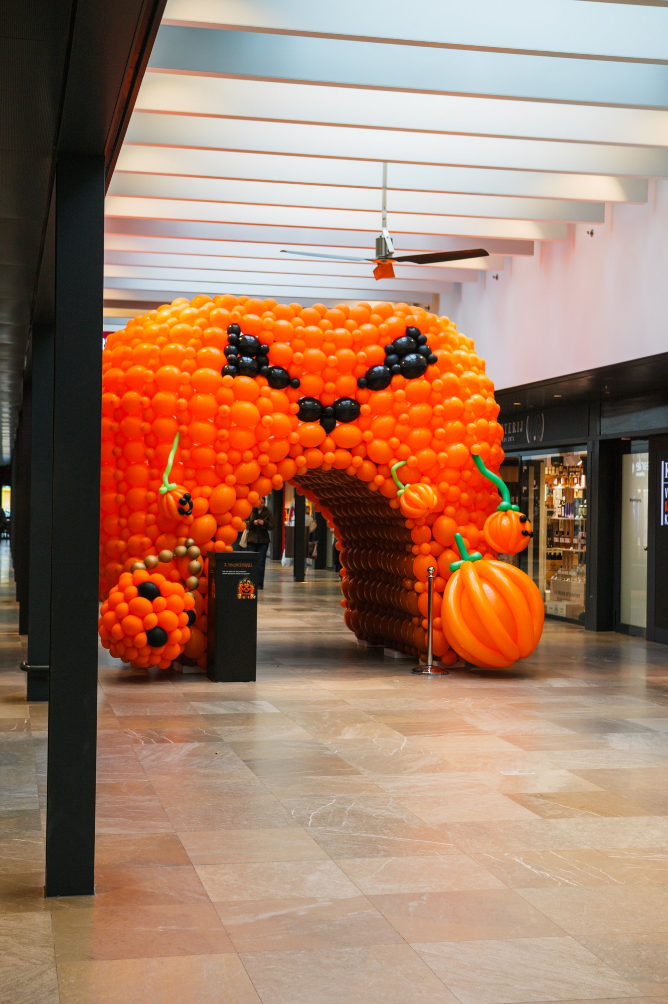 Orange balloon pumpkin tunnel across a walkway at Gelderlandplein (2026) — Design: Wim Vogel — Photo: zestien:negen
