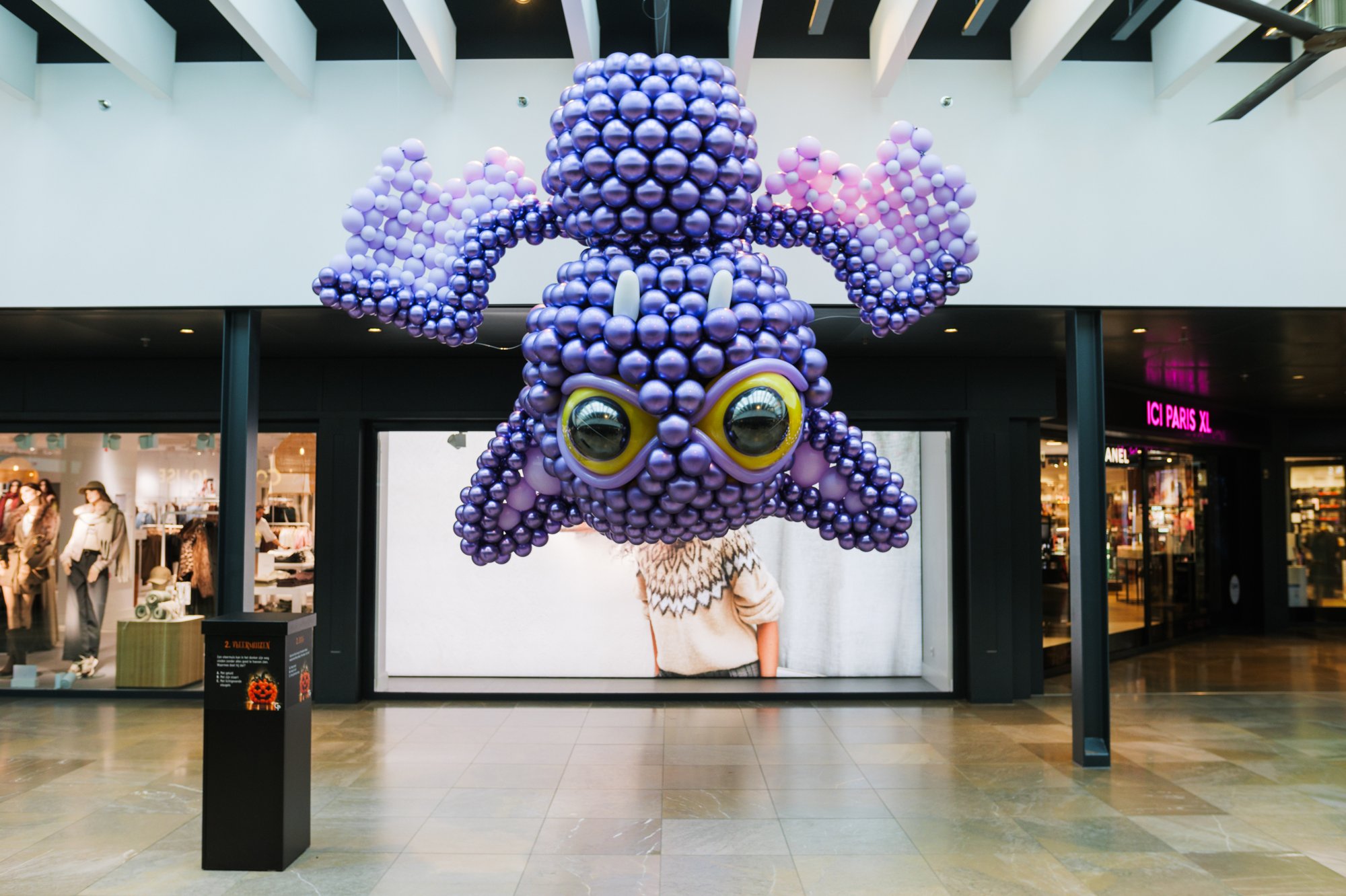 Purple balloon bat hanging upside down at Gelderlandplein (2026) — Design: Wim Vogel — Photo: zestien:negen